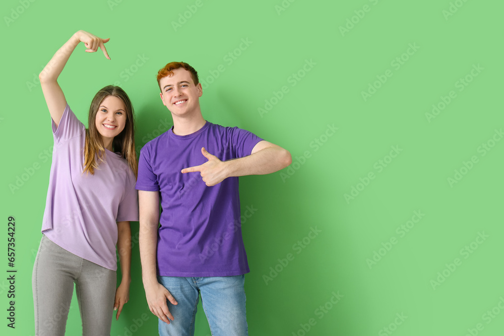 Young couple pointing at their t-shirts on green background