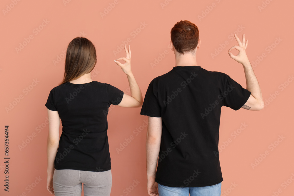 Young couple in black t-shirts showing OK on beige background, back view