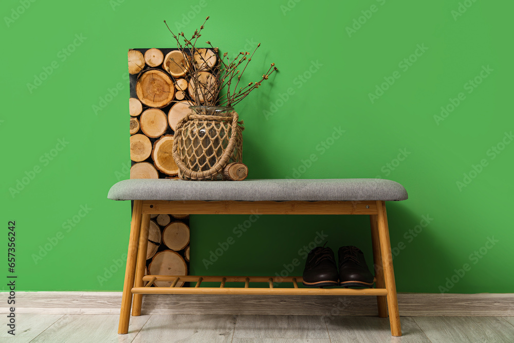 Soft bench with vase and shoes near green wall in room