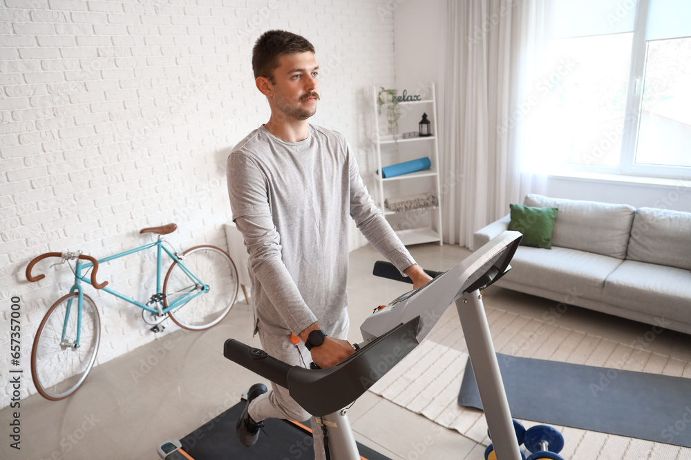 Sporty young man training on treadmill at home