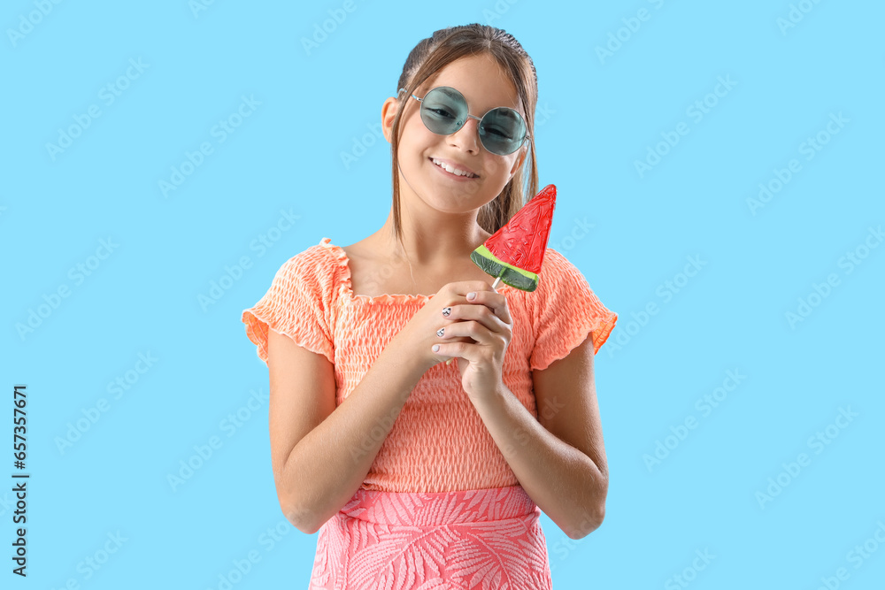 Happy little girl with lollipop in shape of watermelon slice on blue background