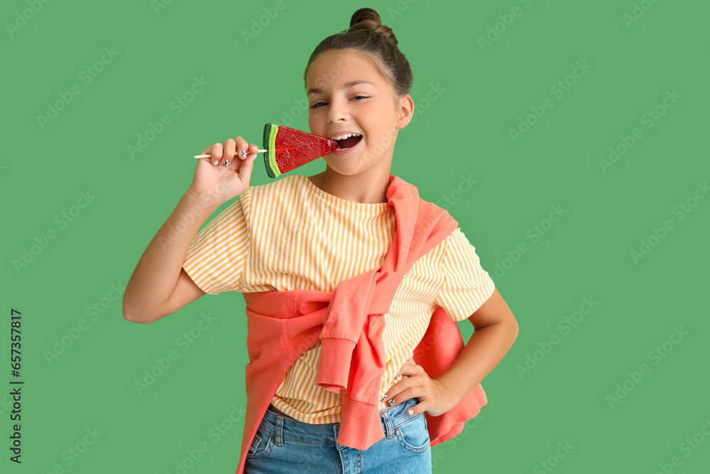 Happy little girl eating lollipop in shape of watermelon slice on green background