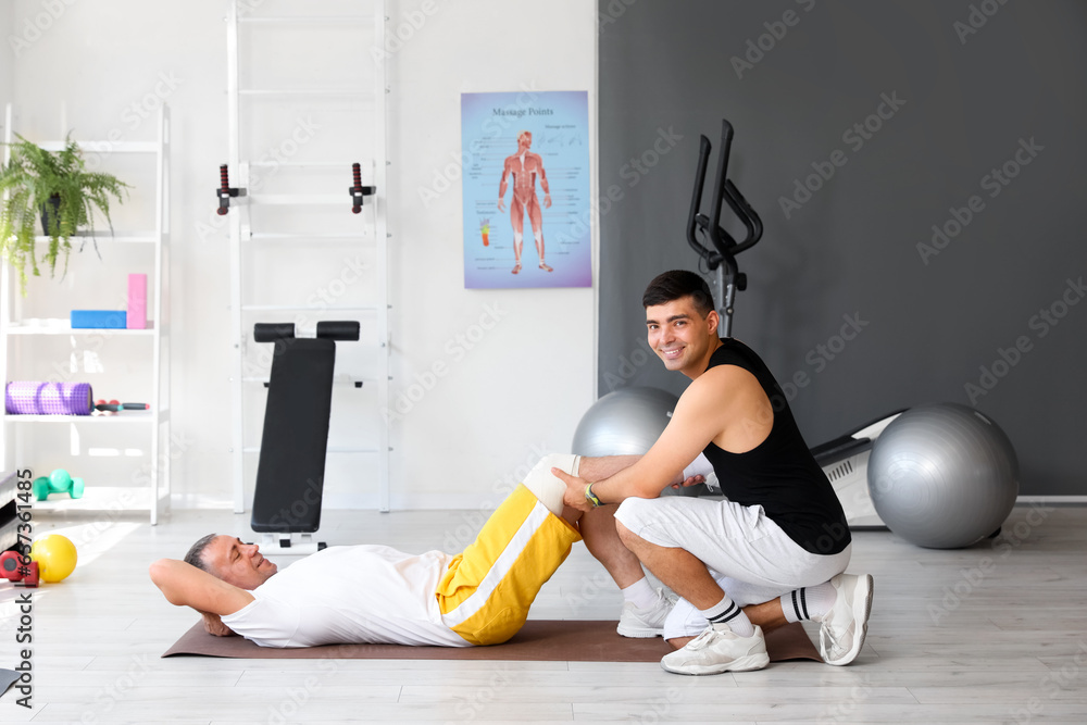 Mature man training on mat with therapist in rehabilitation center