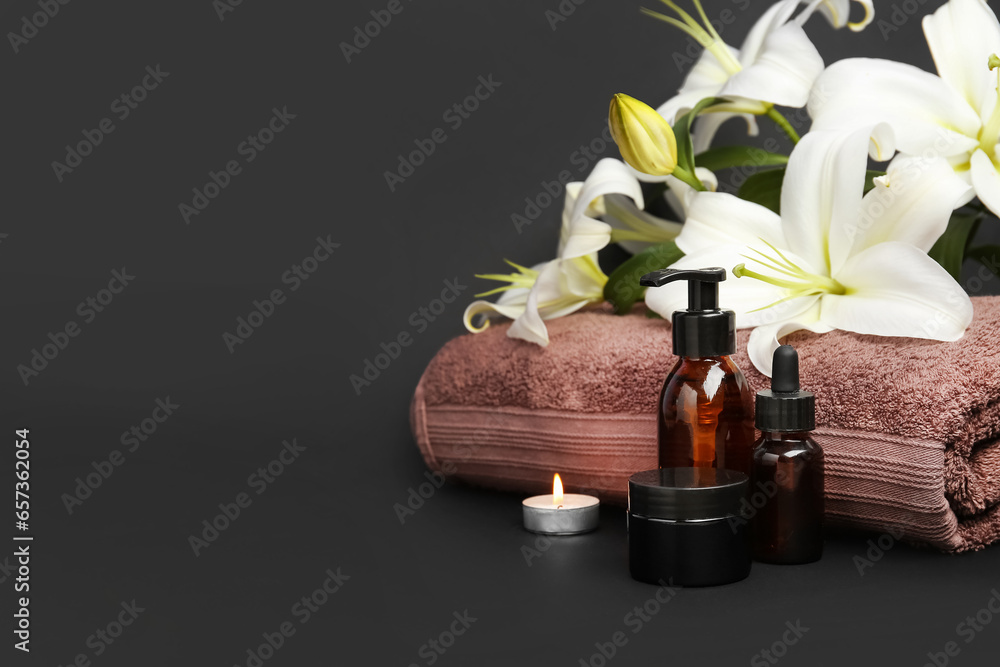 Cosmetic products, clean towel and beautiful lily flowers on dark background