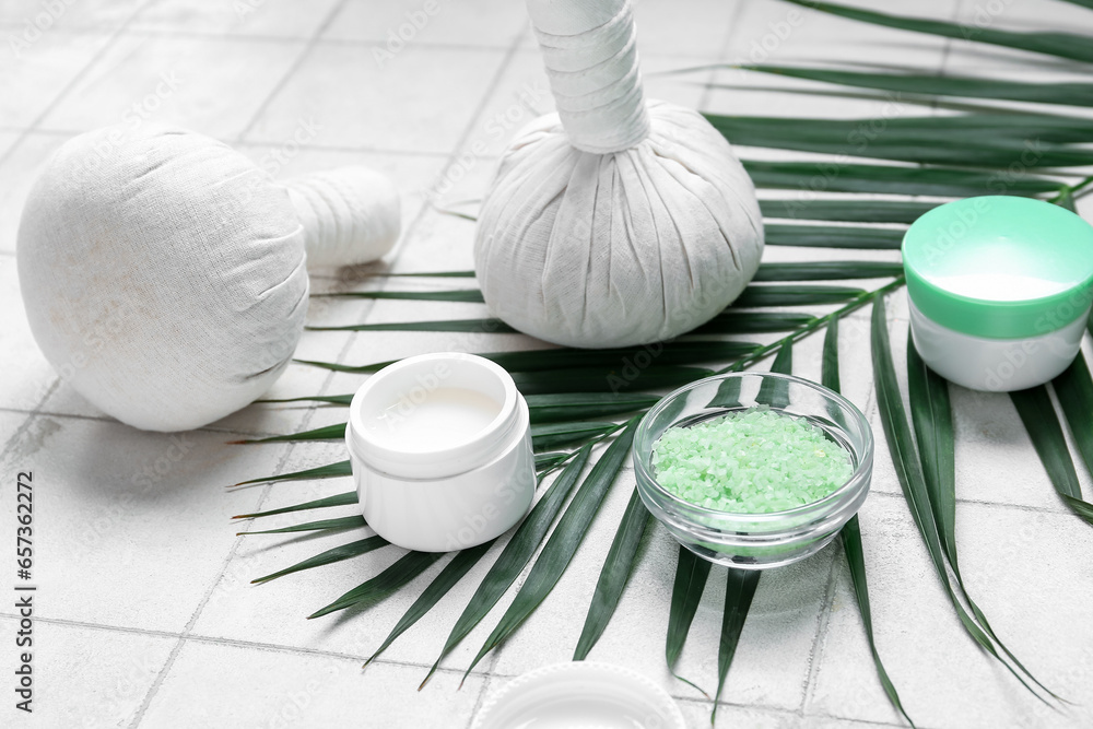 Composition with cosmetic products, herbal massage bags and palm leaf on light tile background