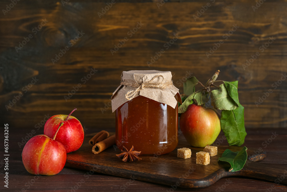 Cutting board with jar of sweet apple jam and ingredients on wooden background