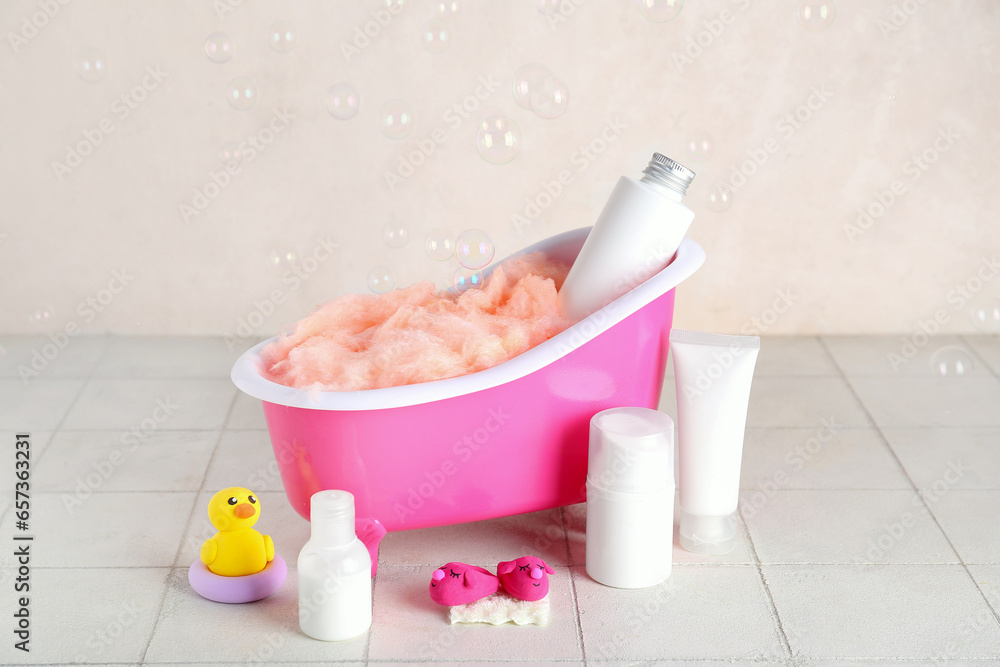 Small bathtub, cosmetic products and soap bubbles on light tile table