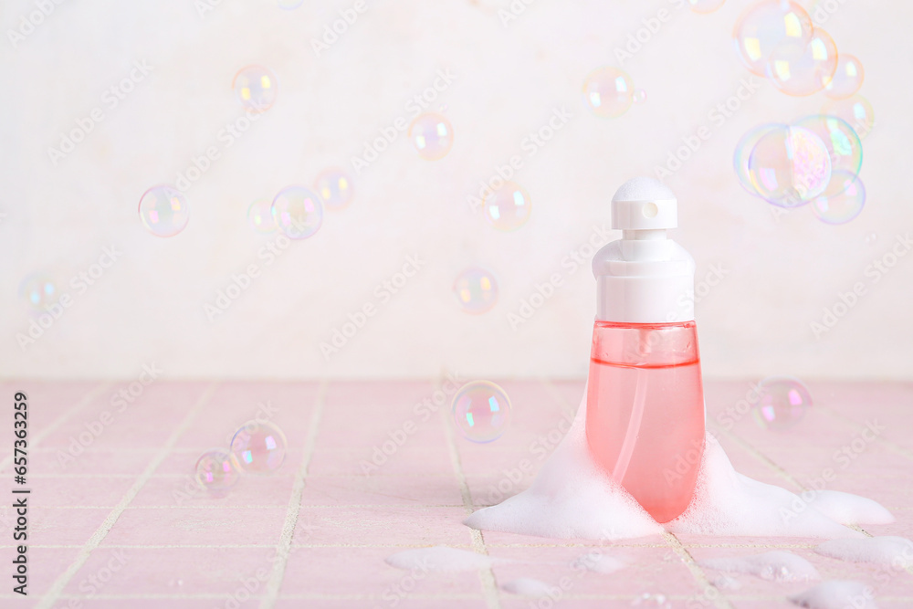 Bottle of cosmetic product with foam and soap bubbles on color tile table against light background