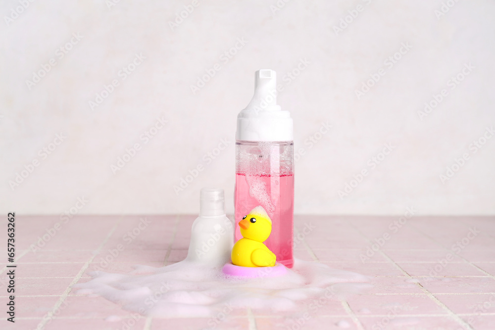 Cosmetic products with foam and duck on color tile table against light background