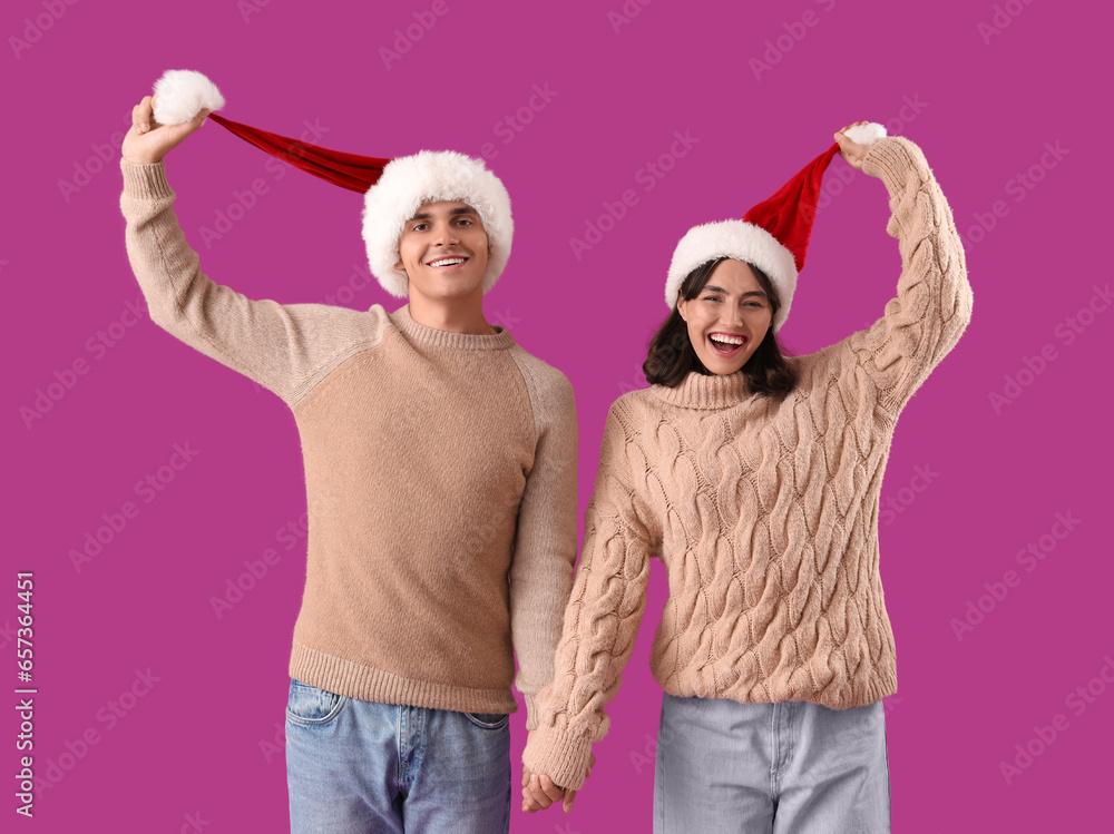 Happy young couple in Santa hats on purple background