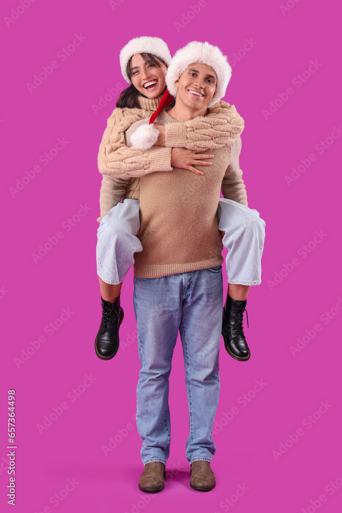 Happy young couple in Santa hats having fun on purple background