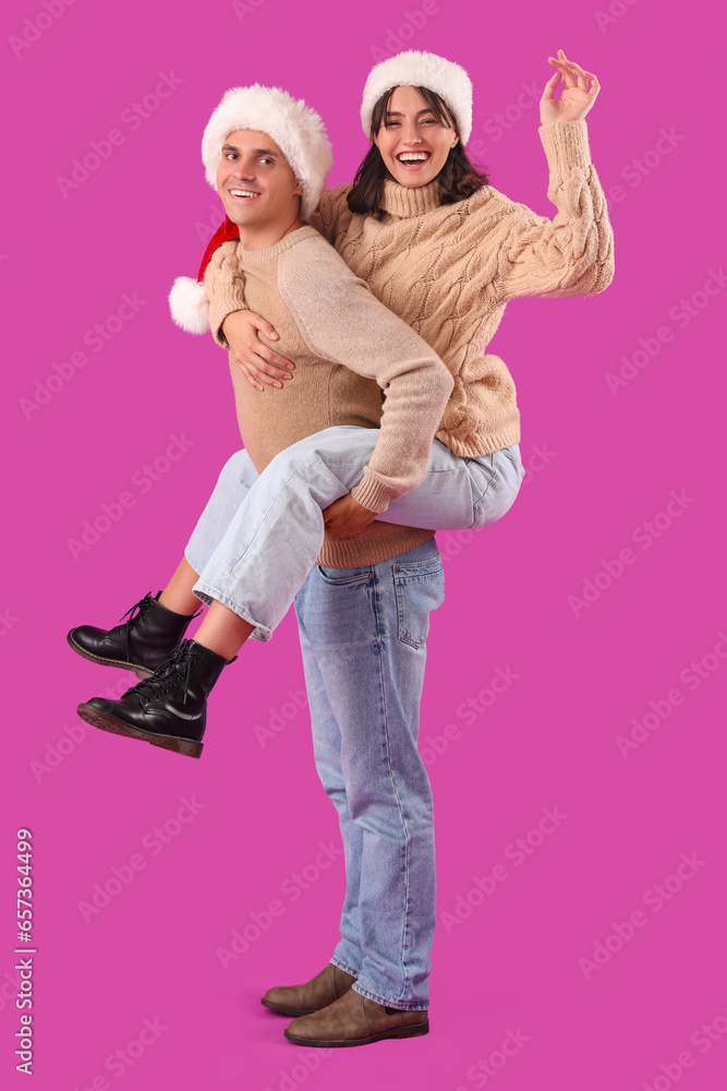 Happy young couple in Santa hats having fun on purple background