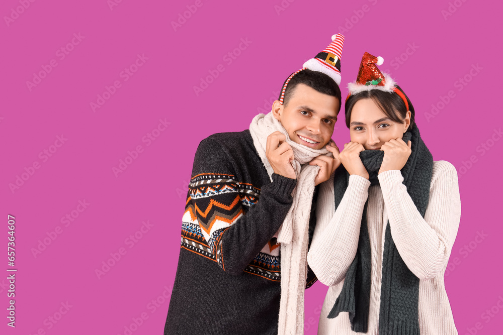 Happy young couple in Christmas hats and warm scarf on purple background