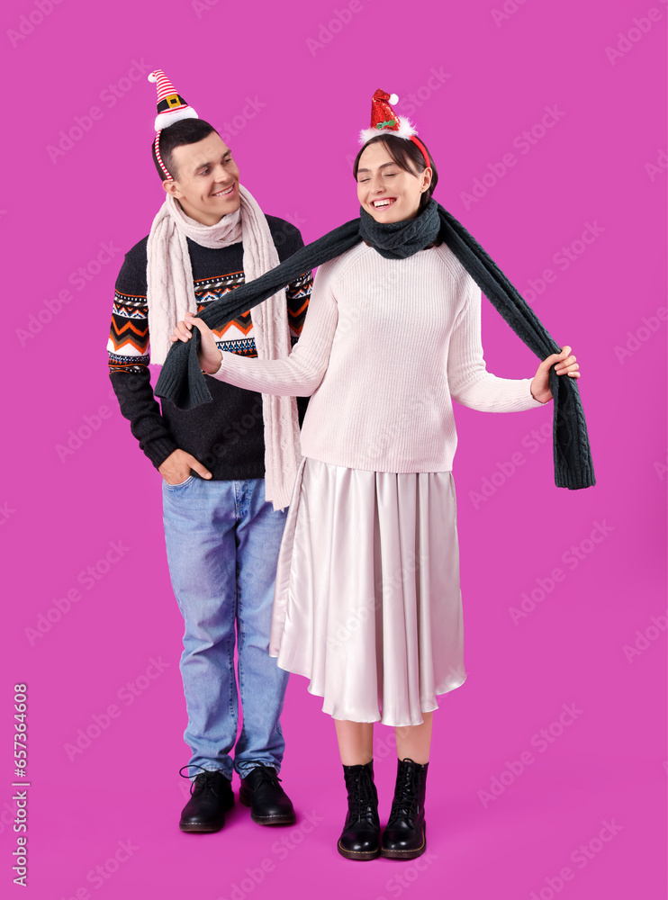 Happy young couple in Christmas hats and warm scarf on purple background