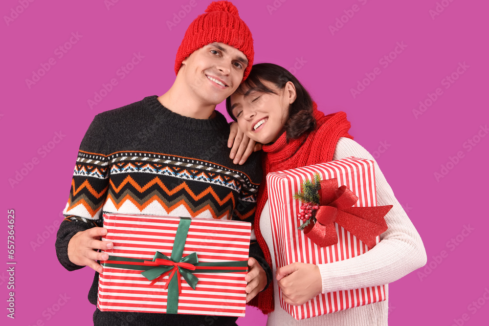 Happy young couple in warm clothes with gift boxes on purple background