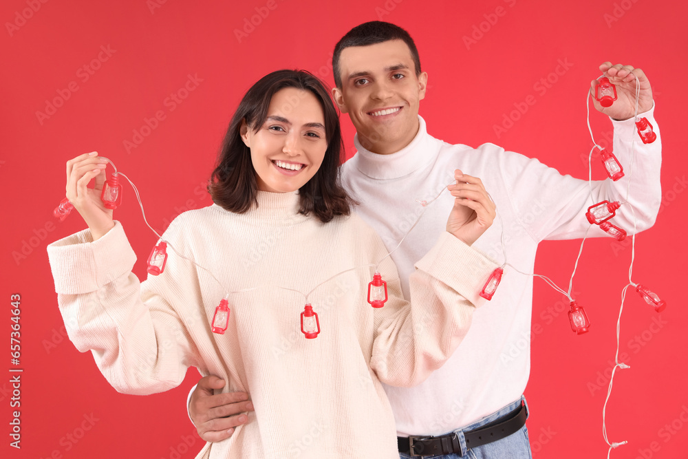 Happy young couple with Christmas garland on red background