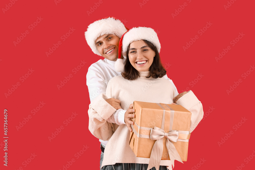 Happy young couple in Santa hats with gift box on red background