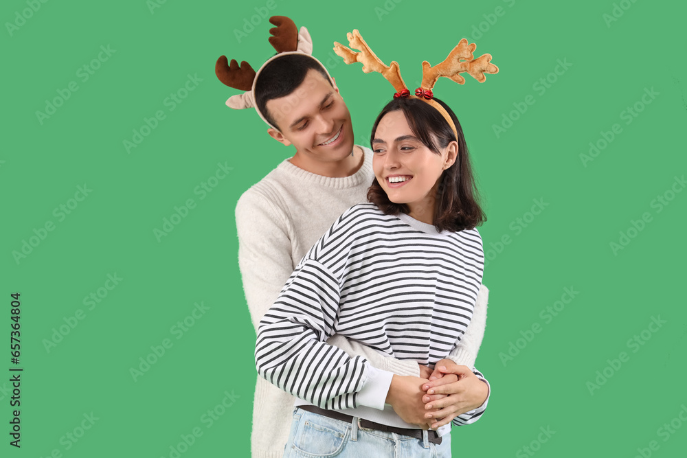 Happy young couple in Christmas reindeer horns hugging on green background