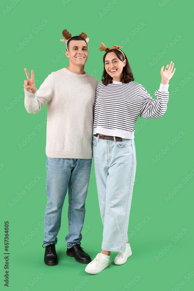 Happy young couple in Christmas reindeer horns on green background