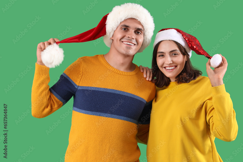 Happy young couple in Santa hats on green background