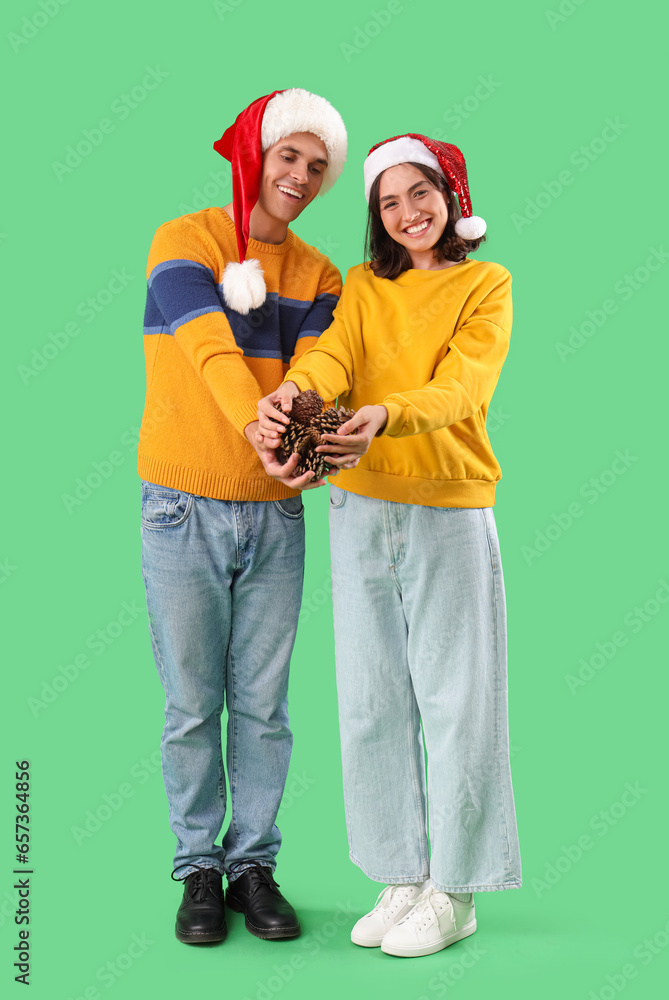 Happy young couple in Santa hats with forest bumps on green background