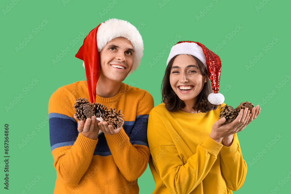 Happy young couple in Santa hats with forest bumps on green background