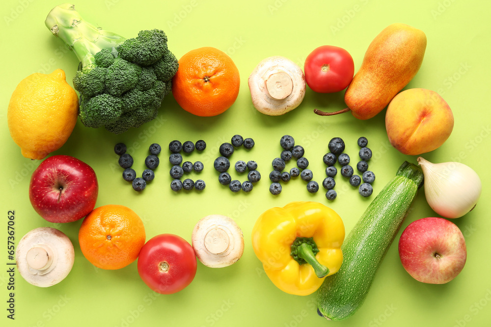 Word VEGAN made of blueberries with different fruits and vegetables on green background