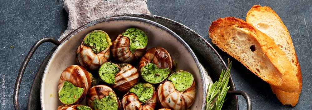 Snails with herbs butter,  French traditional food with parsley and bread on grey background.