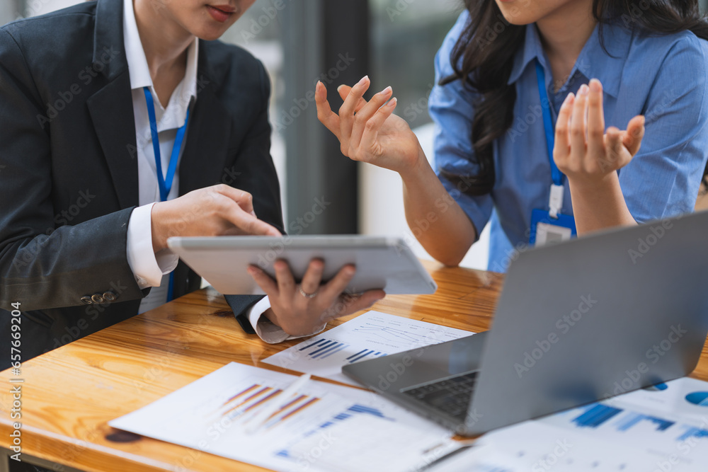 Two Asian businesswomen discuss investment project work and planning strategy Brainstorm together Find information online on iPad Laptop and tablet for making reports and summarizing business results