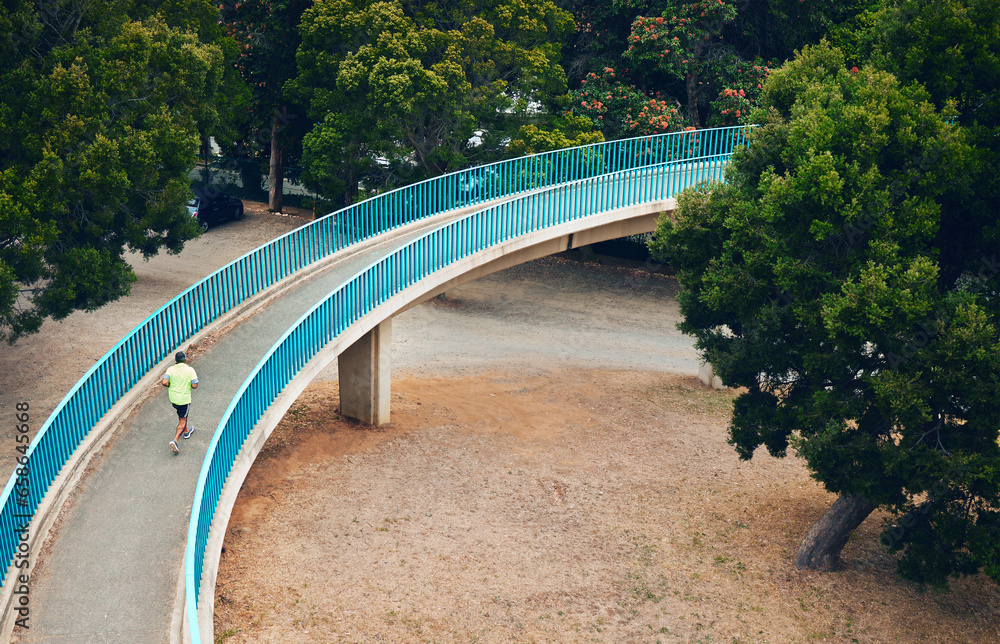 Above, man and running on bridge in nature, countryside or outdoor in environment with path in woods. Athlete, run or walking on road for cardio, fitness or exercise in forest with eco infrastructure