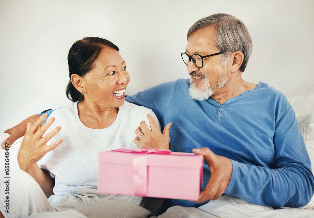 Senior, man and woman with gift in bedroom for anniversary, romantic or together. Asian, elderly couple and bond by smile in happiness for celebration by surprise expression on face, embrace and love