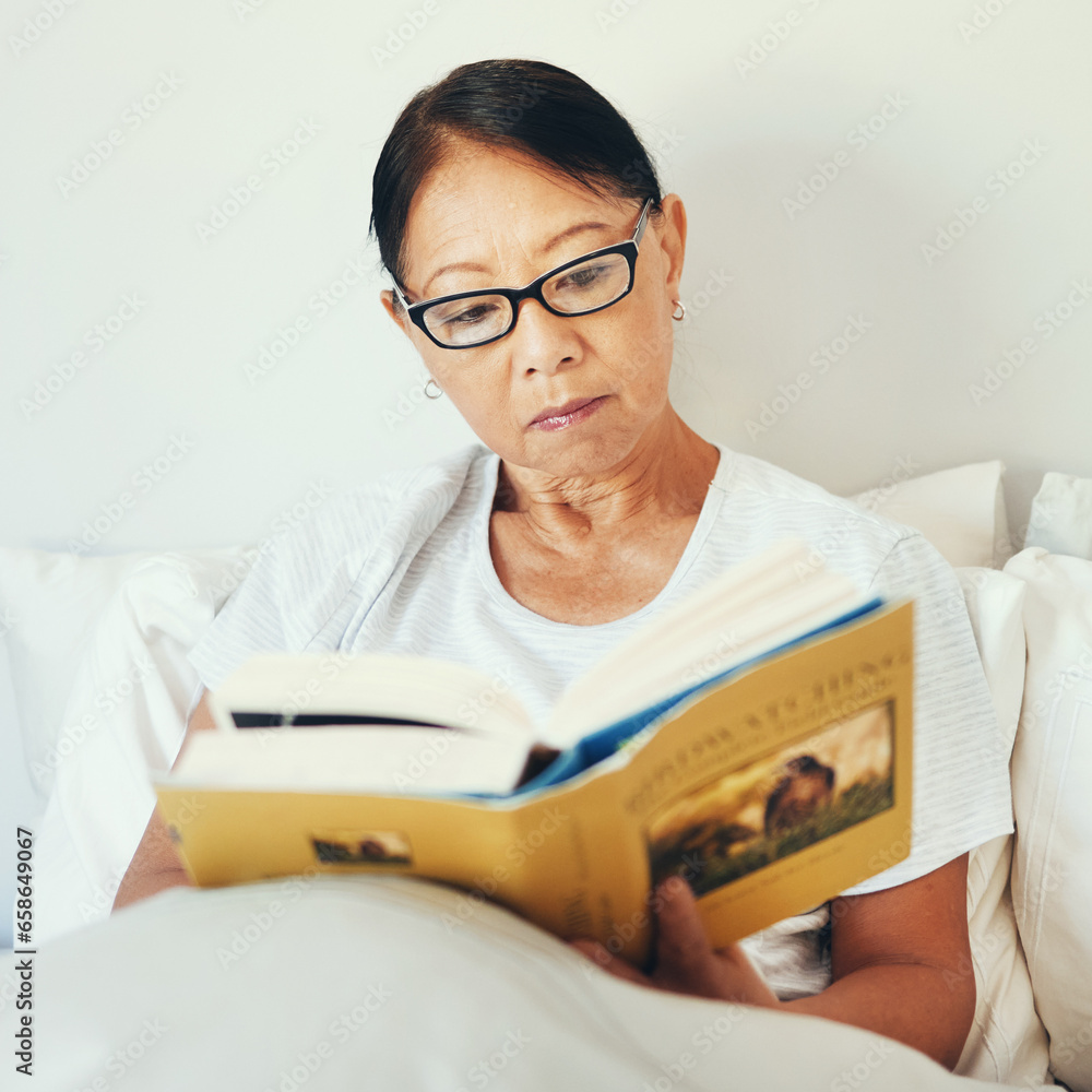 Mature woman reading books in bedroom for story, fiction novel and knowledge at home. Serious asian person, glasses and comfortable in bed with literature for rest, hobby and relax to enjoy break