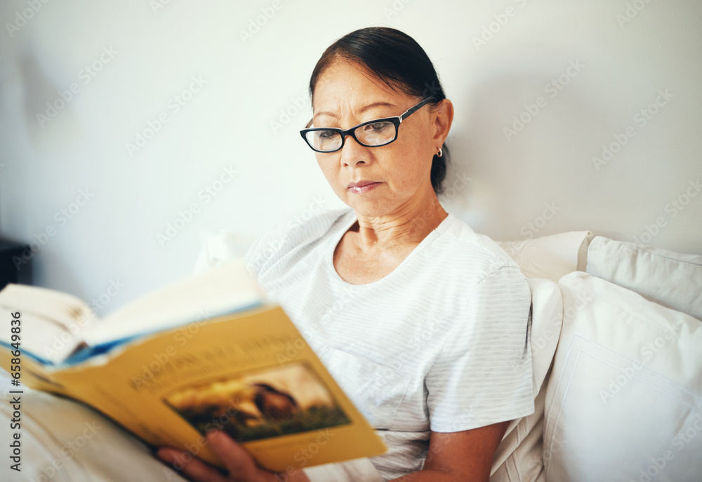 Serious, woman and reading books in bedroom for story, fiction novel and knowledge at home. Mature asian person, glasses and comfortable in bed with literature for rest, hobby or relax to enjoy break