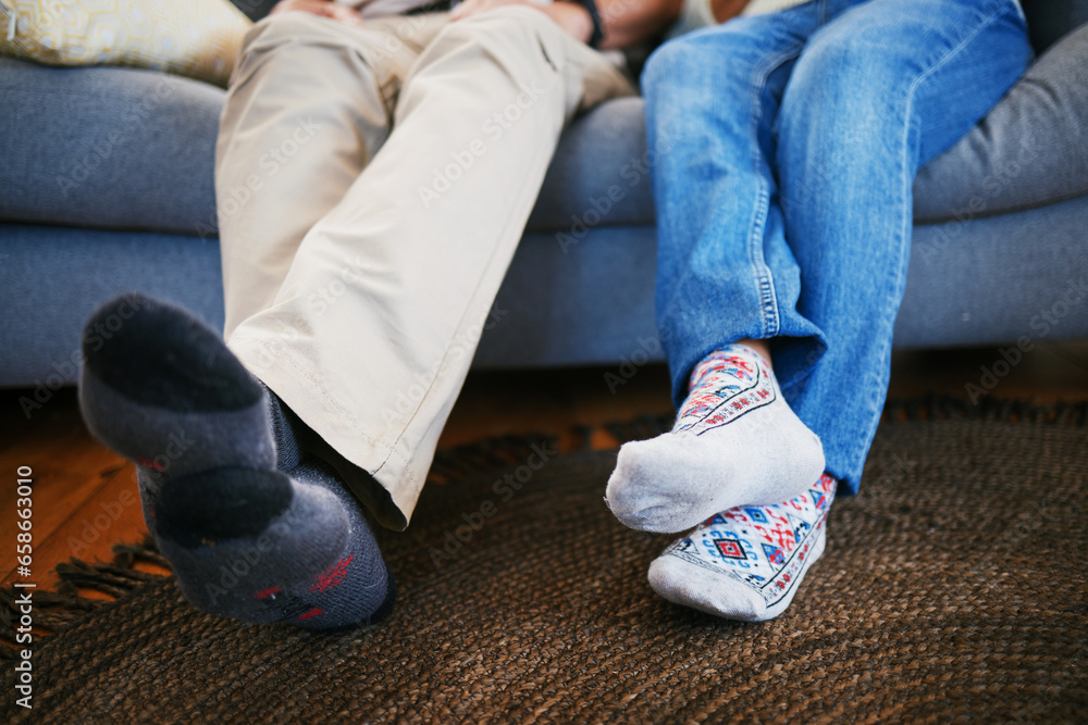 Legs, feet in socks and a couple on a sofa in the living room of their home together closeup to relax. Love, relationship and bonding with people in their house for a break on weekend in winter