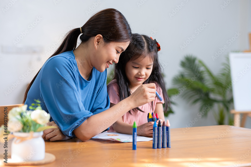 A young family spends their free time together in the living room at home. Mother and little daughter draw pictures with crayons on paper, smiling happy.