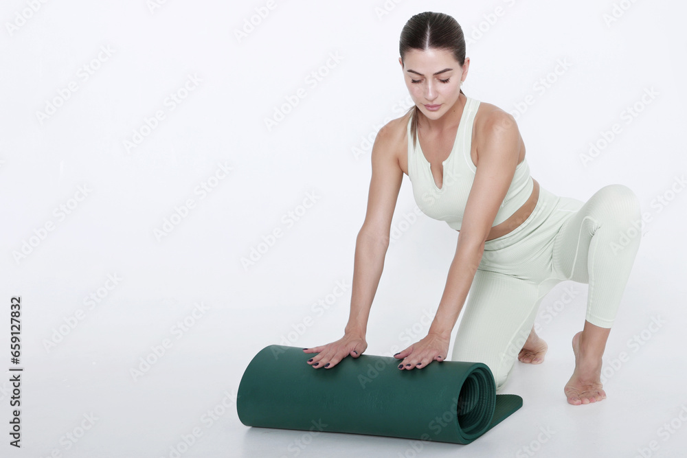 An attractive young woman lays out yoga or fitness mat. Healthy lifestyle. Isolated object. Copy space.