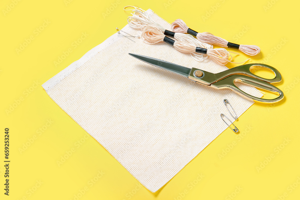 Canvas with scissors, mouline threads and pins on yellow background