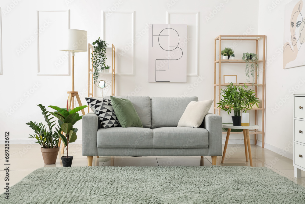 Interior of light living room with cozy grey sofa and green houseplants