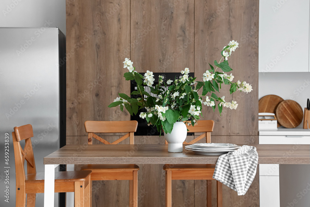 Vase with blooming jasmine flowers on wooden table in modern kitchen