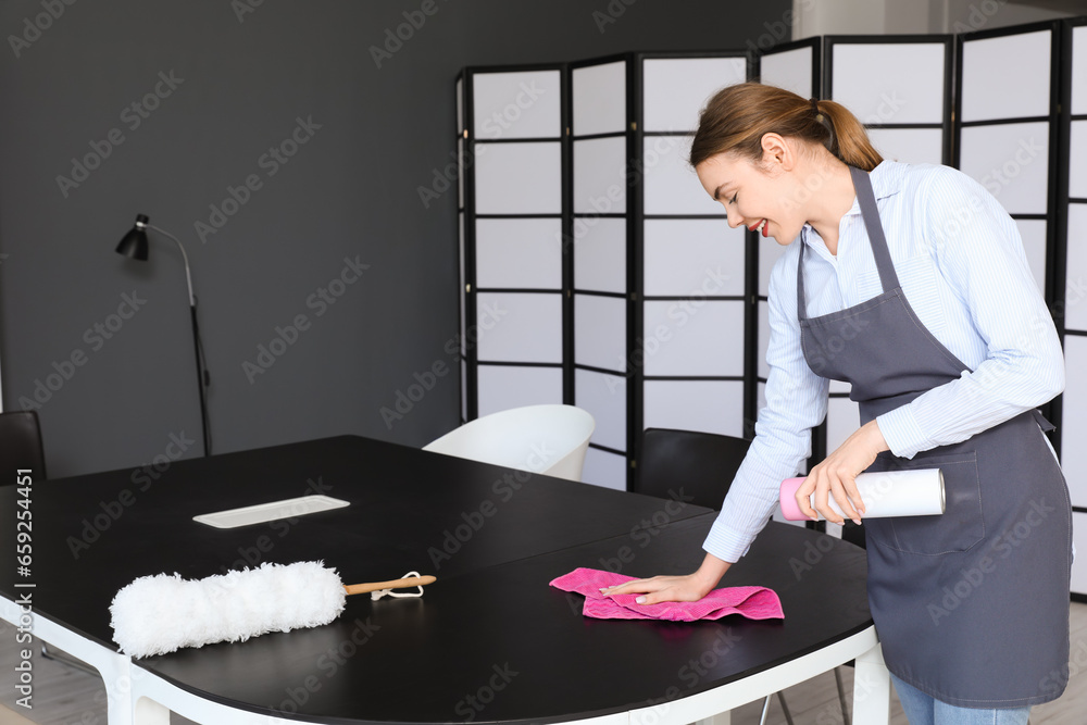 Female janitor cleaning table in office