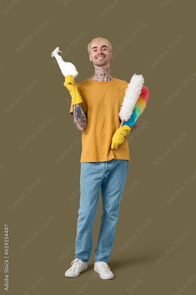 Young tattooed man with bottle of detergent and pp-dusters on green background