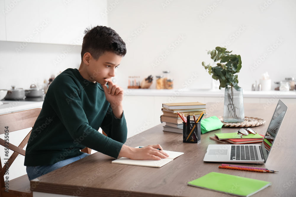 Little boy studying online with laptop in kitchen