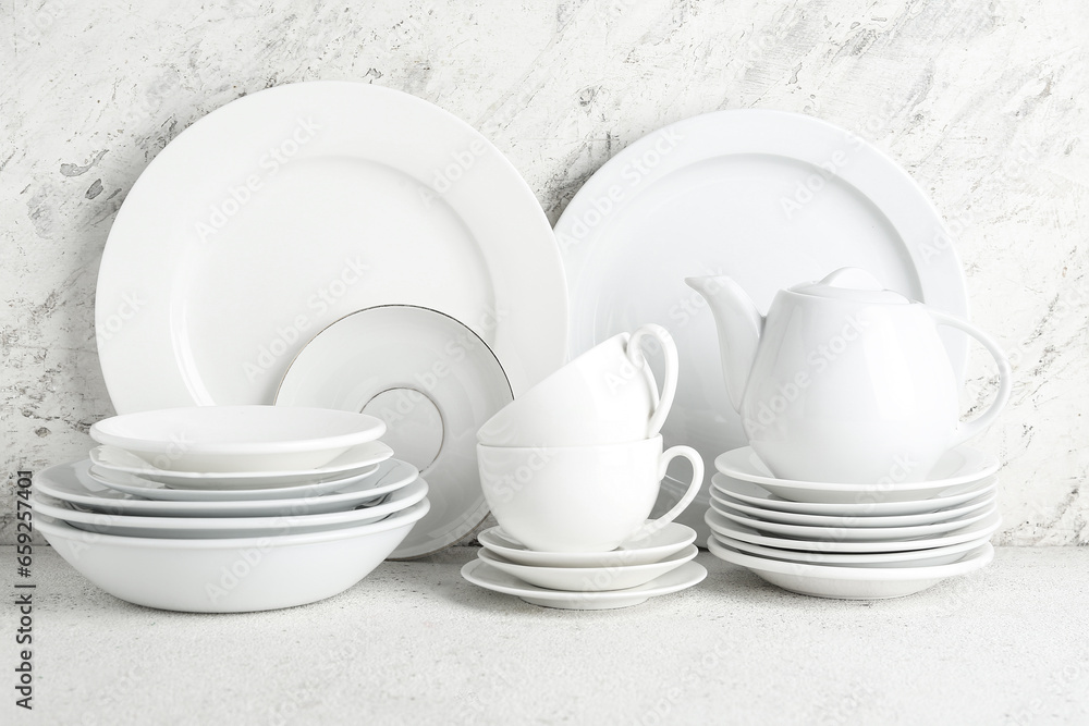 Set of clean plates, cups, teapot and saucers on white table