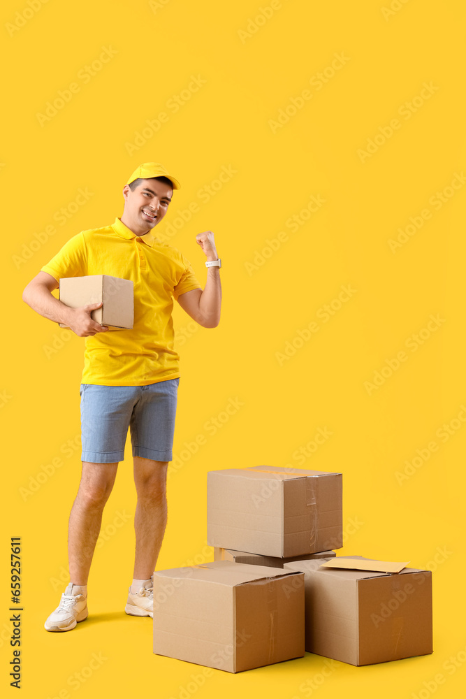 Happy male courier with parcels on yellow background