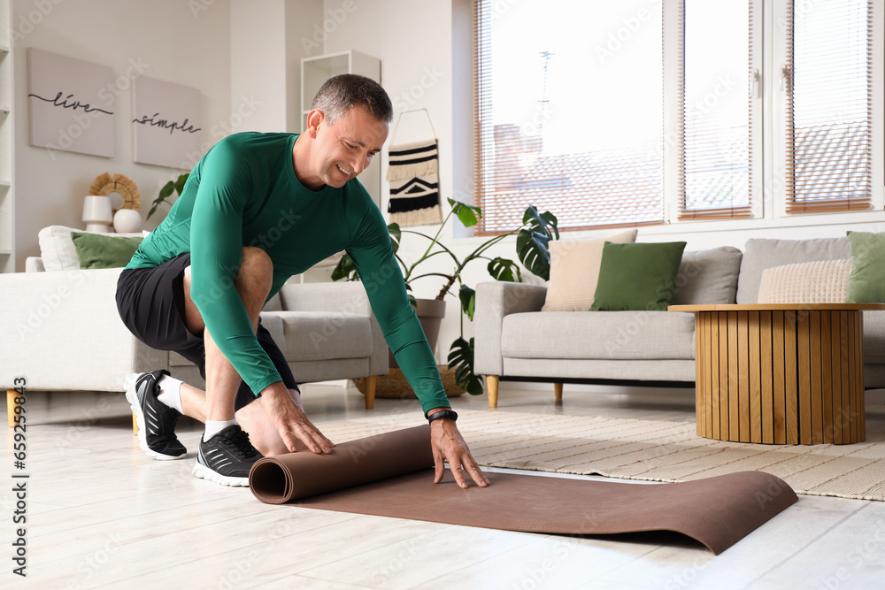 Sporty mature man rolling out fitness mat at home