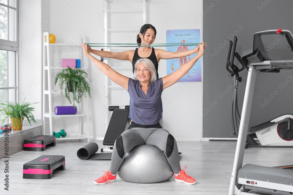 Mature woman training with therapist on fitball in rehabilitation center