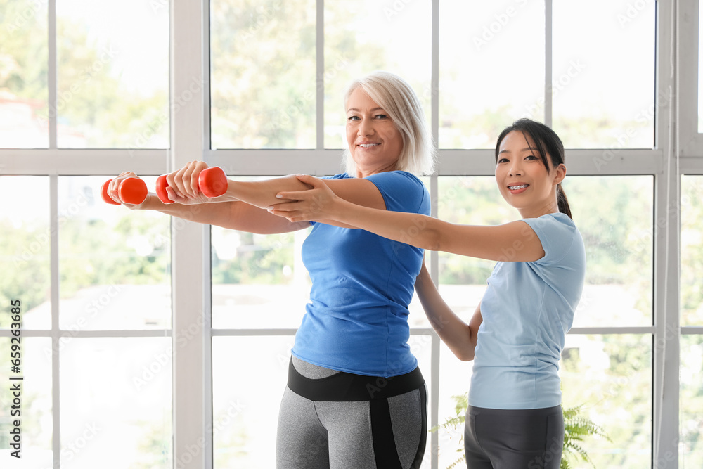 Mature woman training with dumbbells and therapist in rehabilitation center