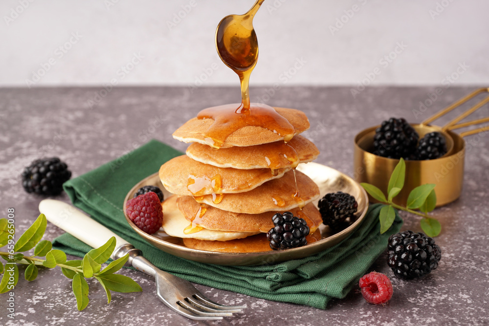 Pouring of maple syrup onto tasty pancakes with berries on table