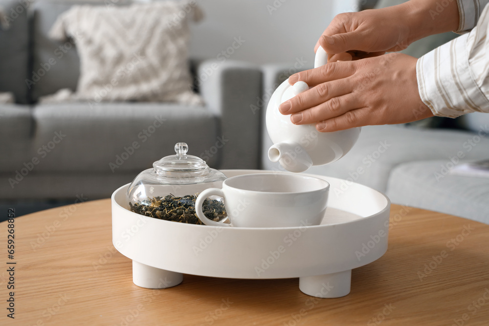 Young woman pouring hot tea into cup at home, closeup