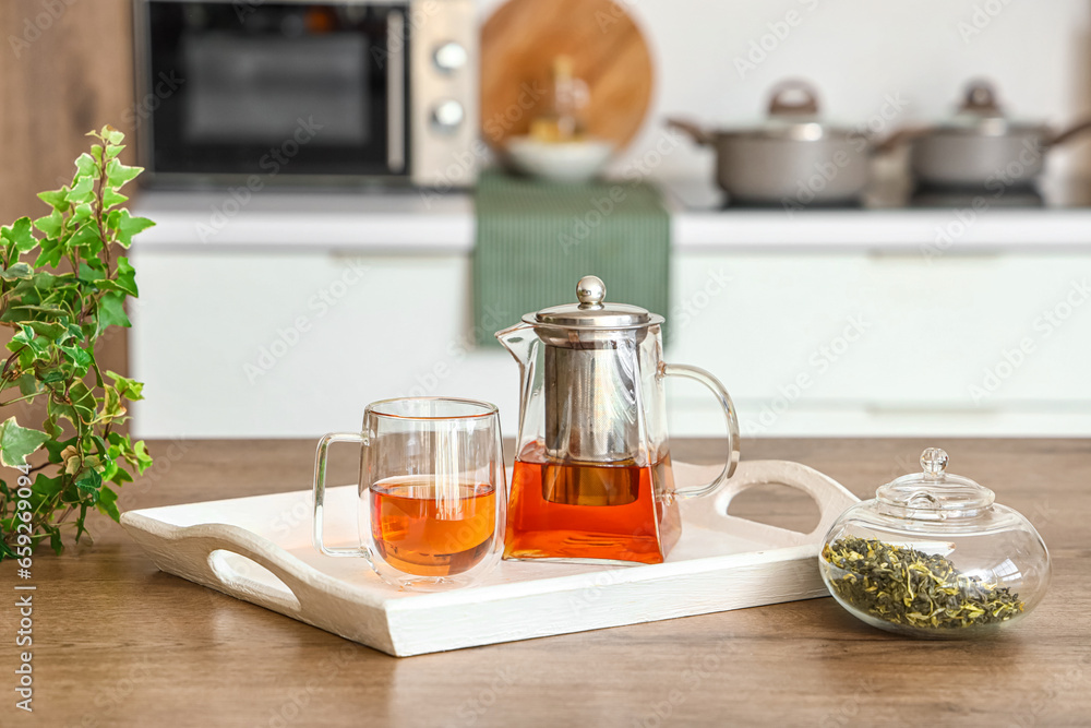 Tray with teapot and glass cup on table in kitchen